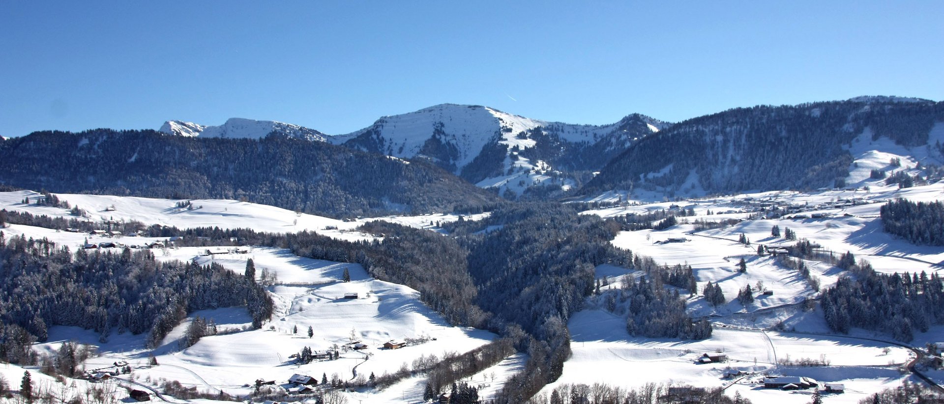 Winterlandschaft mit schneebedeckten Bergen und Häusern unter klarem blauem Himmel