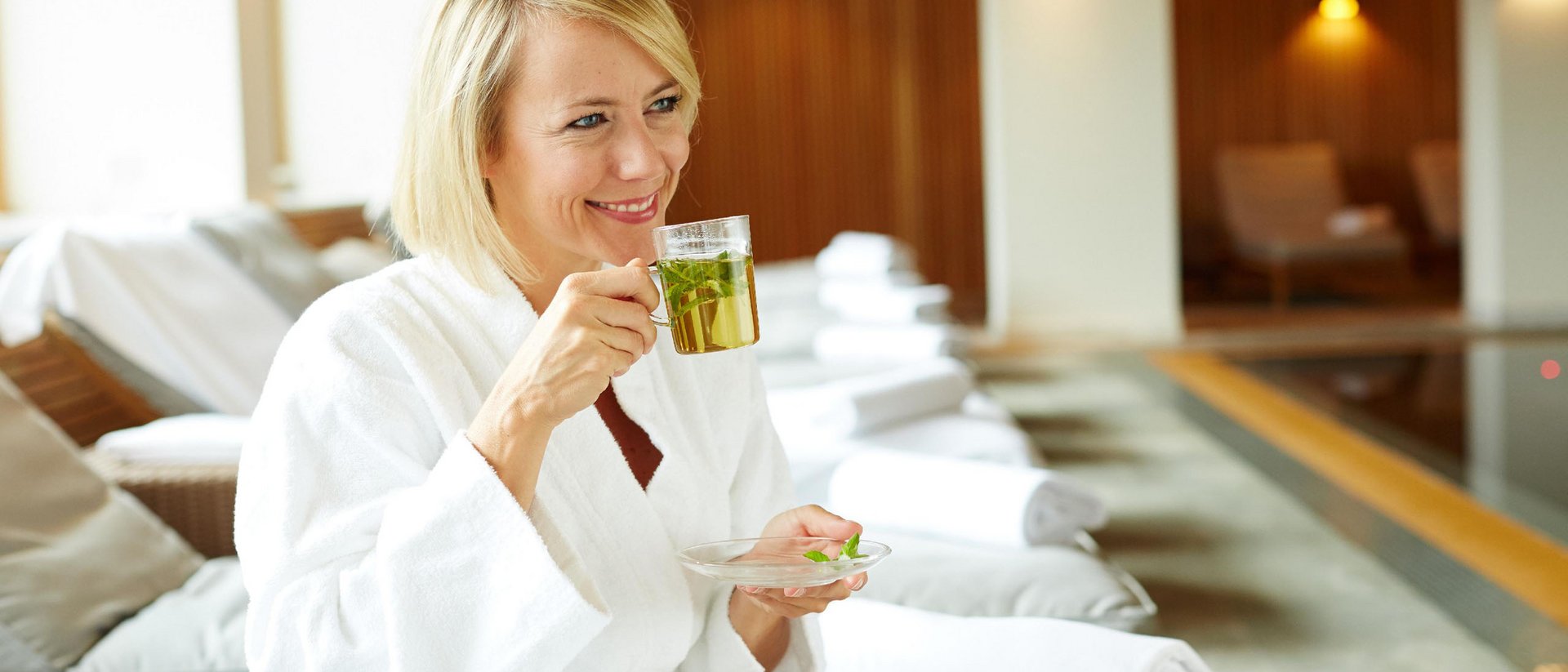 Frau im Bademantel trinkt grünen Tee im Spa-Bereich