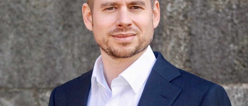 Porträt eines Mannes in blauem Anzug und weißem Hemd vor grauer Wand