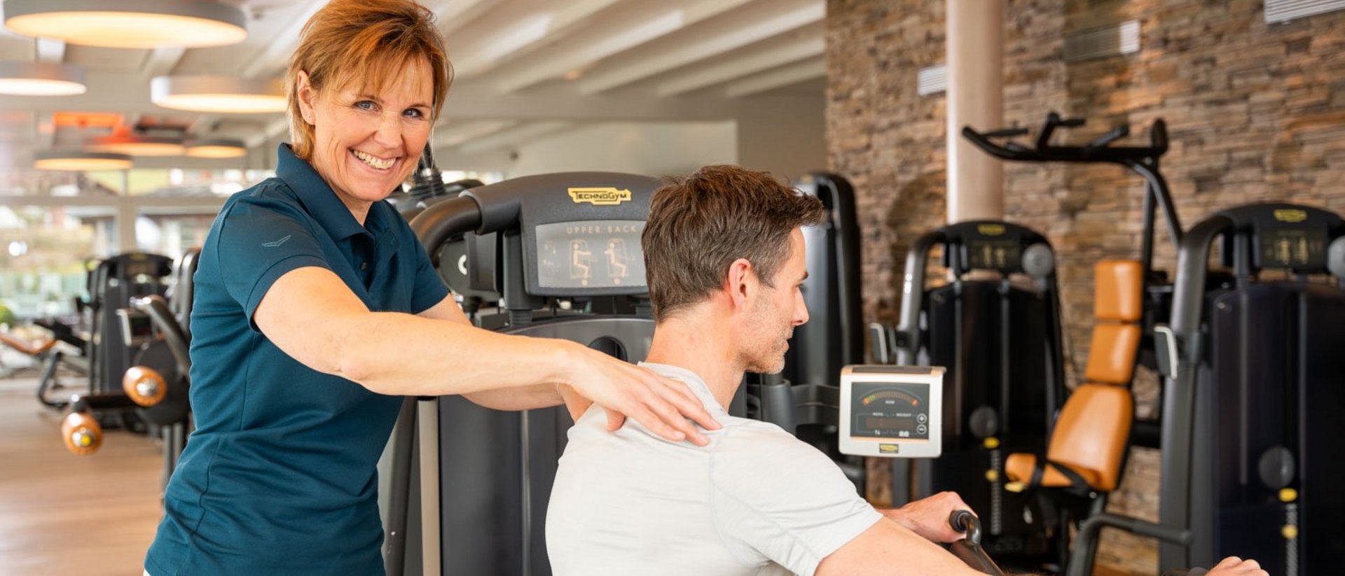 Prevention and rehabilitation at our hotel in Oberstaufen Female trainer assists a man exercising on a fitness machine