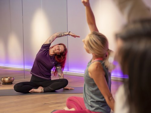 Yoga-Gruppe übt im Sitzen eine seitliche Dehnung im Kursraum