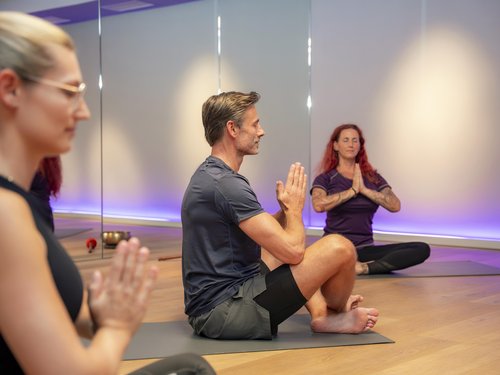 People sitting cross-legged meditating in a yoga studio with dim lighting.