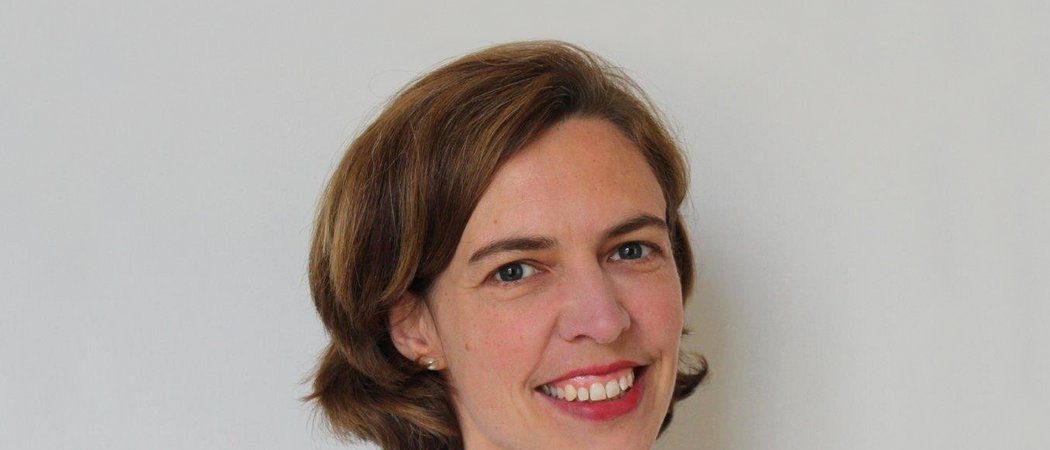 Porträt einer lächelnden Frau mit kurzem braunem Haar und weißem Hemd vor weißem Hintergrund