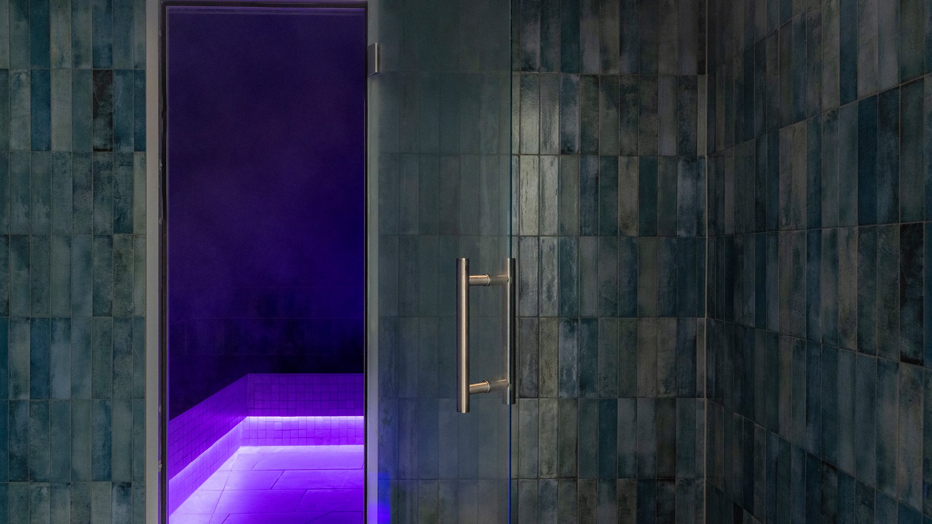 Dampfbad mit offenen Glastüren und violetter LED-Beleuchtung auf hellen Fliesen