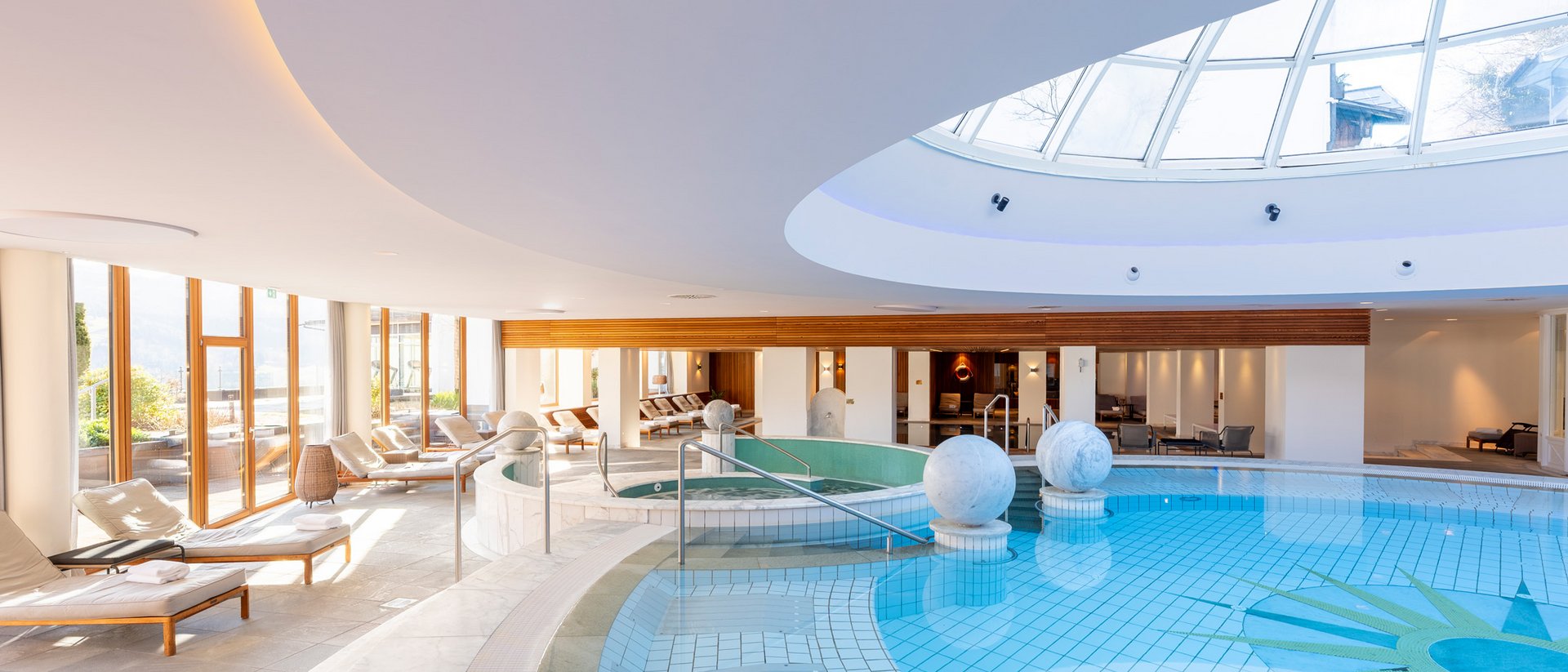 Heller Wellnessbereich mit Pool, Liegestühlen und großer Oberlichtkuppel