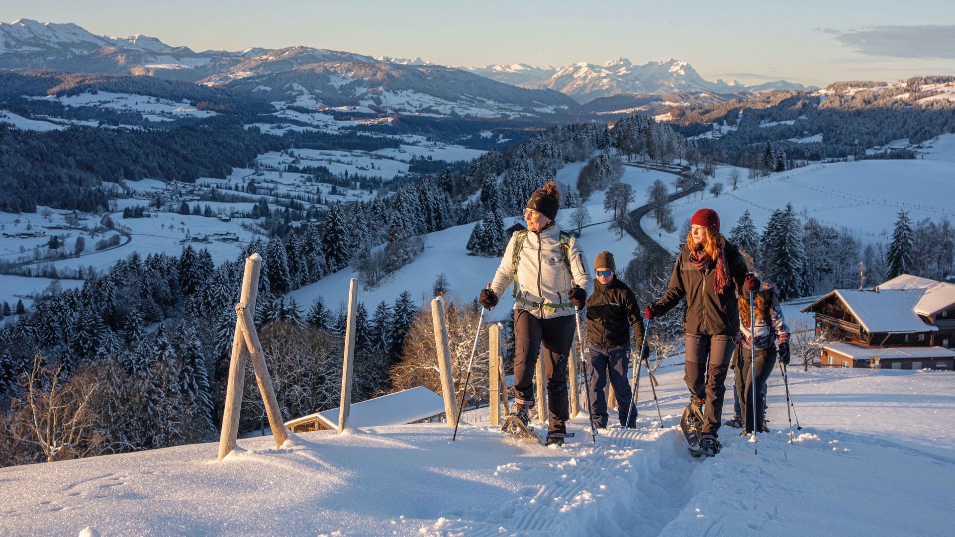 Gruppe beim Schneeschuhwandern in verschneiter Berglandschaft bei Sonnenuntergang