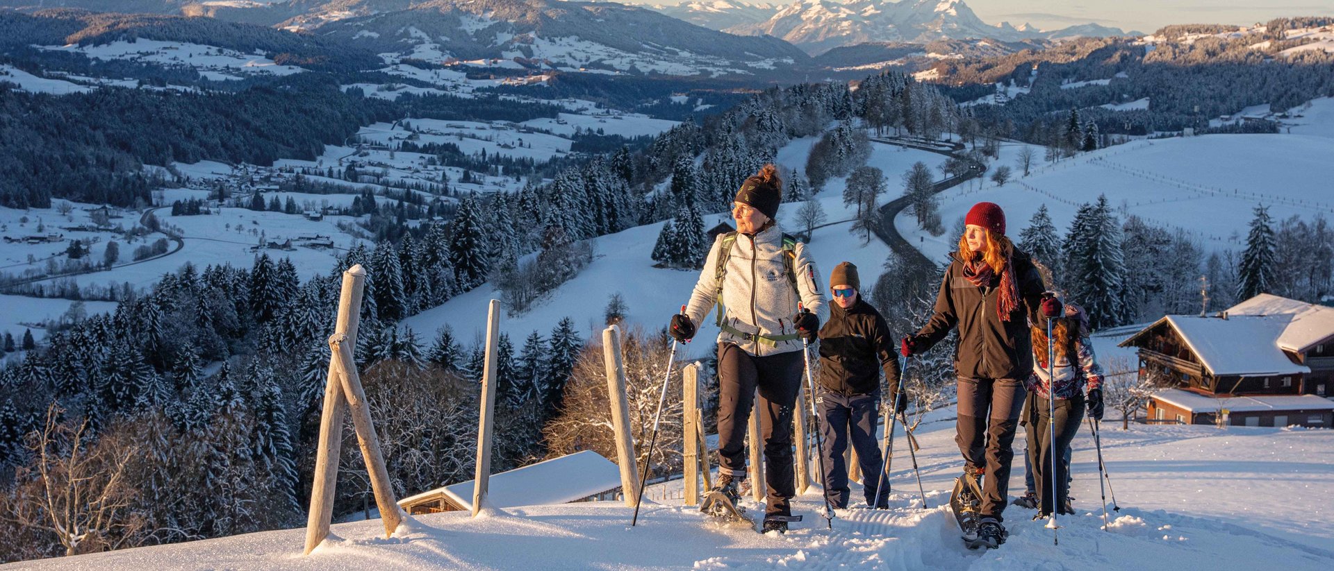 Gruppe beim Schneeschuhwandern in verschneiter Berglandschaft bei Sonnenuntergang